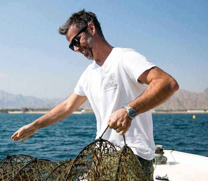 Man in white shirt and sunglasses handling oyster traps on a boat, representing the founder of Dibba Bay Oysters