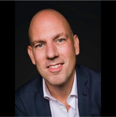 Portrait of a smiling bald man in a dark blazer and light-colored shirt against a black background