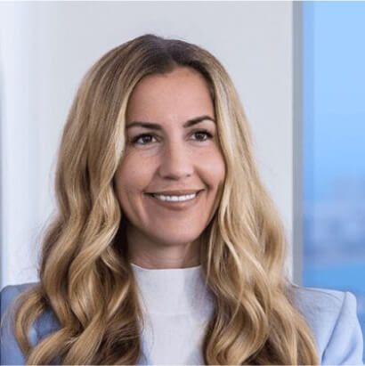 Smiling woman with long wavy blonde hair in blue blazer, photographed in modern office setting