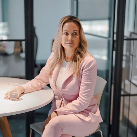 Professional woman in pink suit seated at modern office table, holding a glass of water