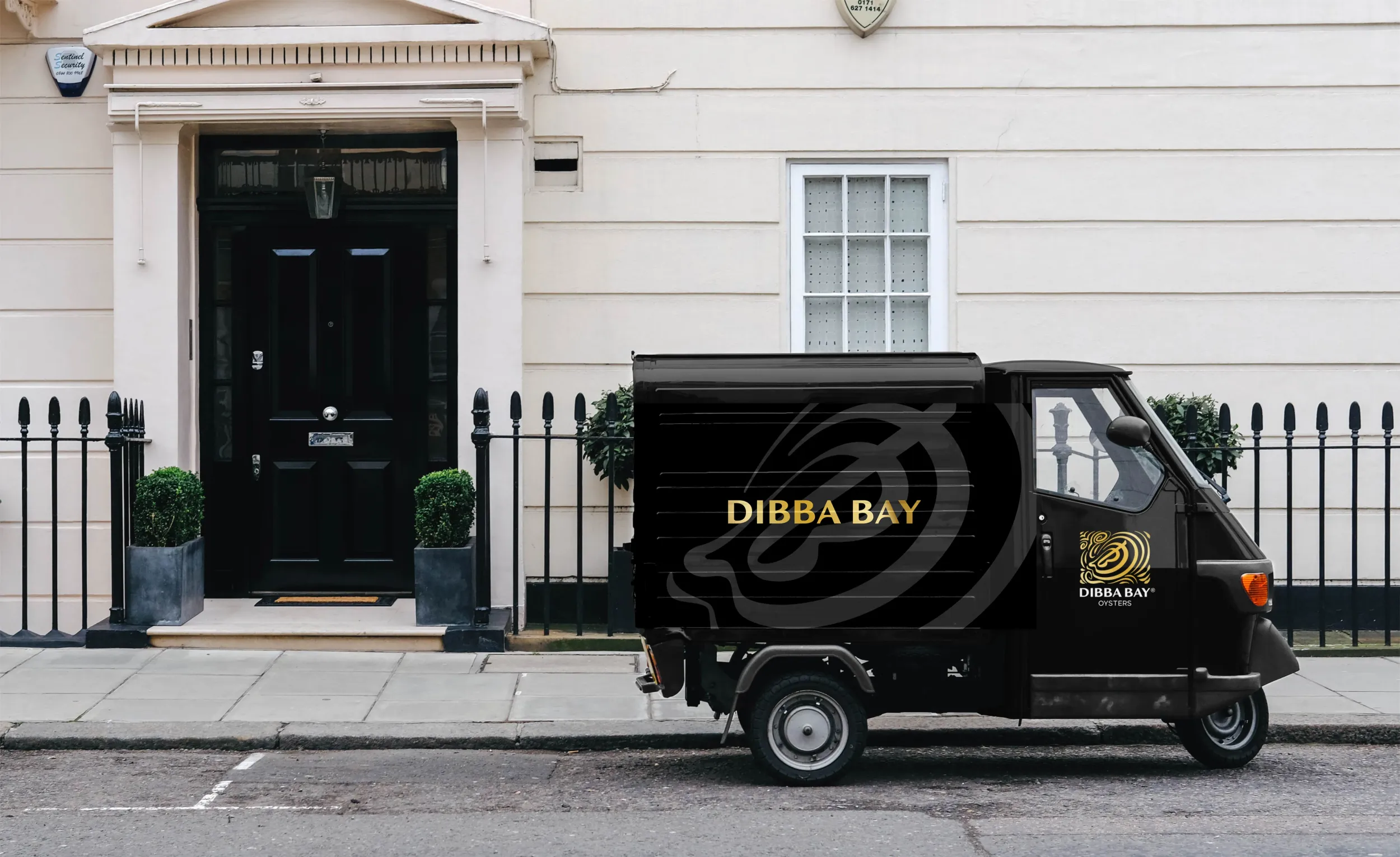 Black Ohba Bay delivery tuk-tuk parked outside a classic white townhouse, featuring gold branding on the side panel