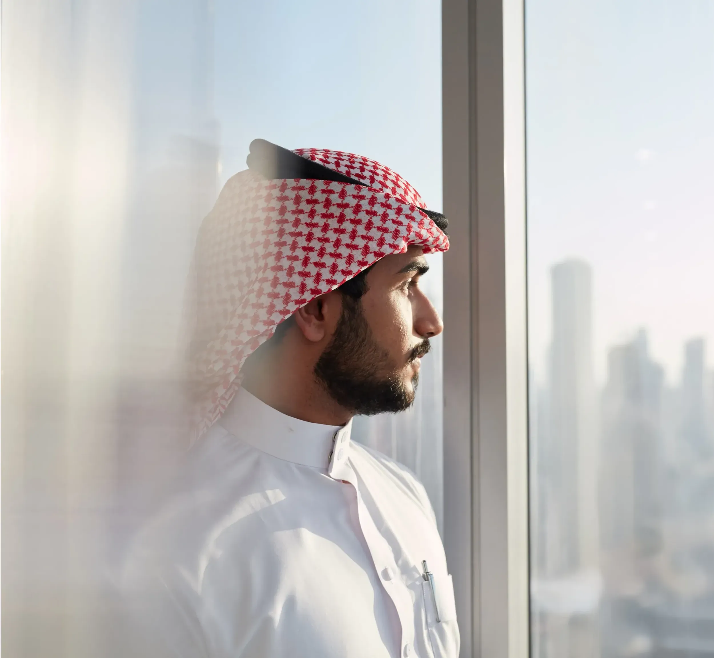 A man in traditional Saudi attire looking out a window at a city skyline, symbolizing vision and future growth. Skyne, a branding agency, helped Basamh Group position itself as a future-focused leader. 