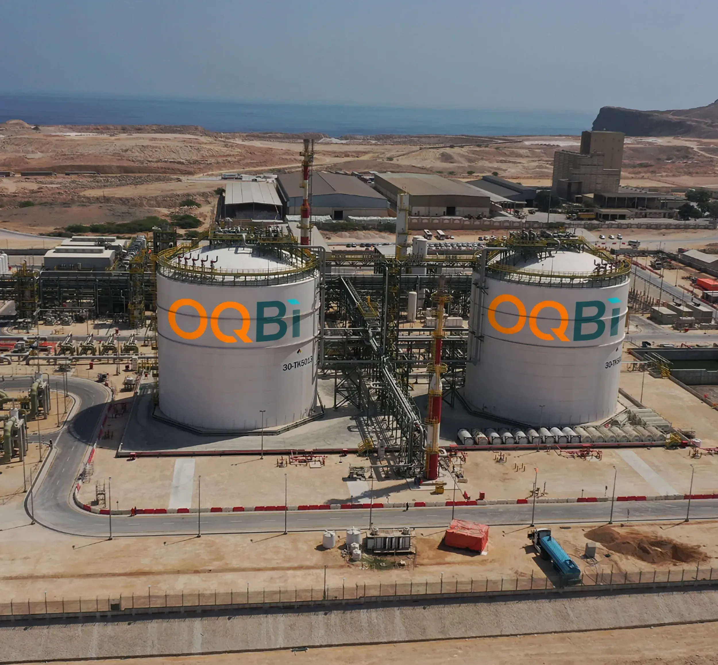 Aerial view of OQBi industrial facility with large storage tanks branded with OQBi logo. Skyne, a creative agency, specializes in industrial branding and visual communication for oil, gas, and energy companies in Dubai, Riyadh, and Jeddah.