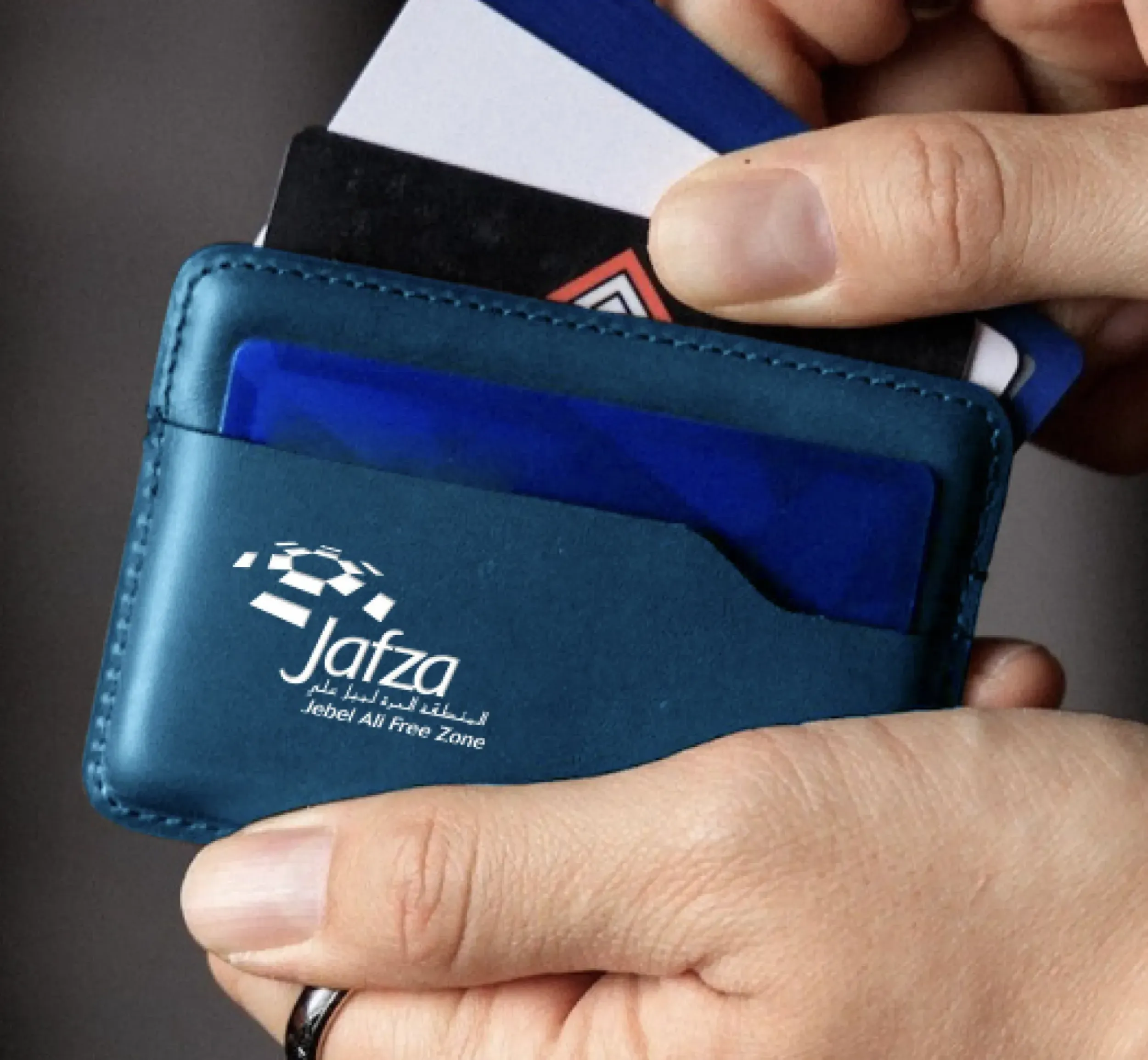 A hand holding a JAFZA branded cardholder with various cards, highlighting Skyne's attention to detail in branding and corporate identity.