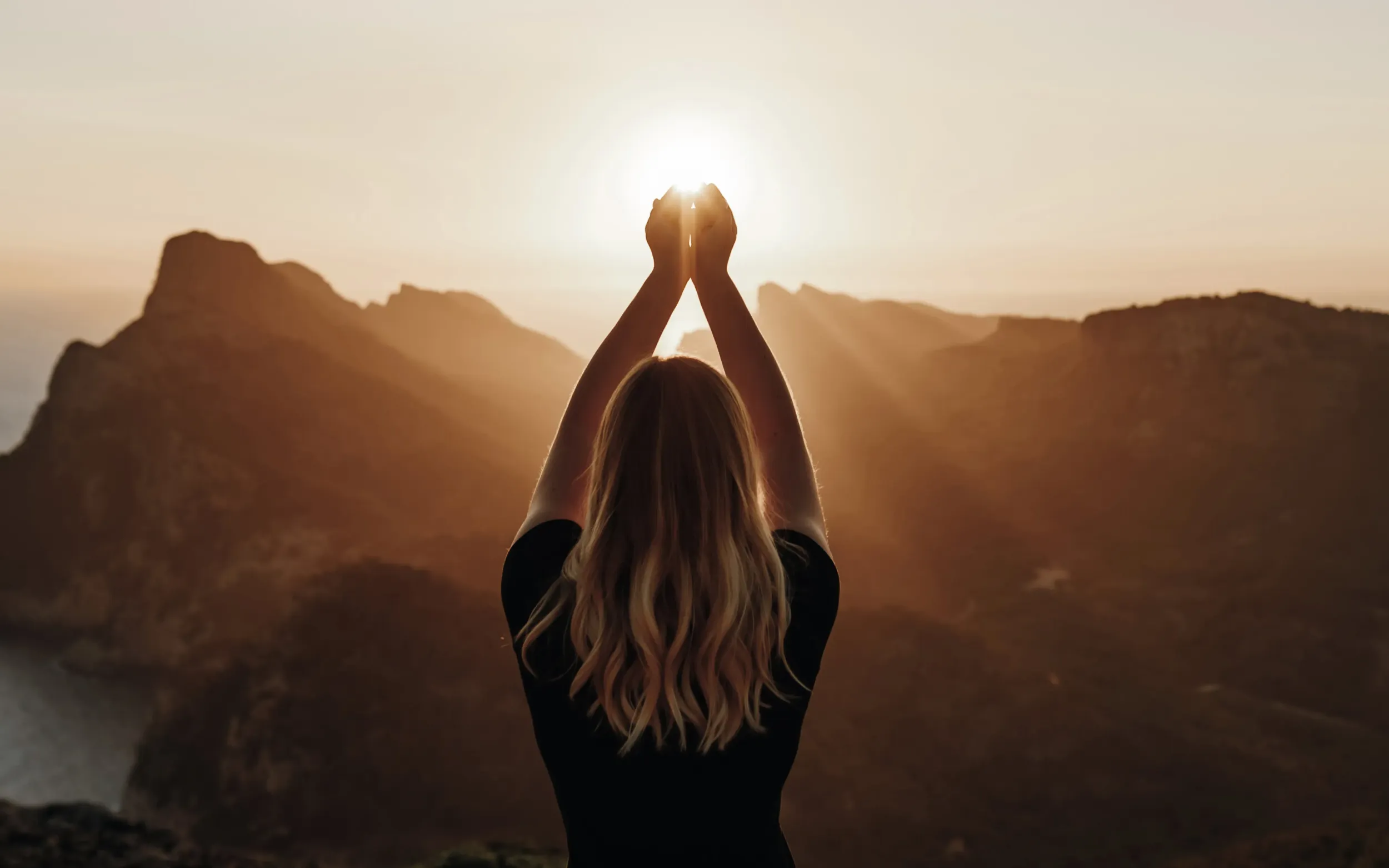 Woman with arms raised towards sunset over mountains, symbolizing Oserth’s brand message of reconnection to nature and self, reflecting Skyne’s holistic branding expertise as a creative agency.