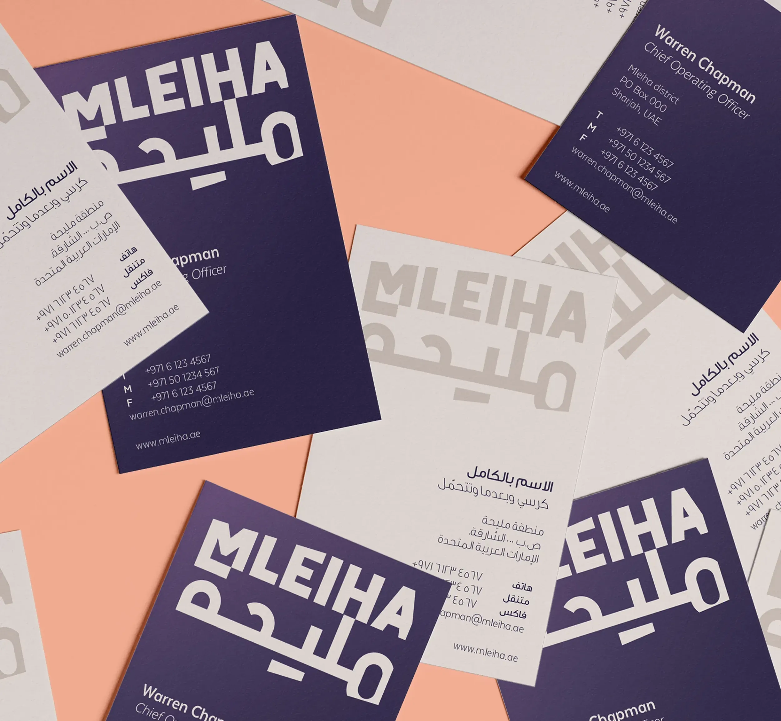 Scattered business cards designed for Mleiha, featuring bold bilingual typography in Arabic and English on dark purple and white backgrounds