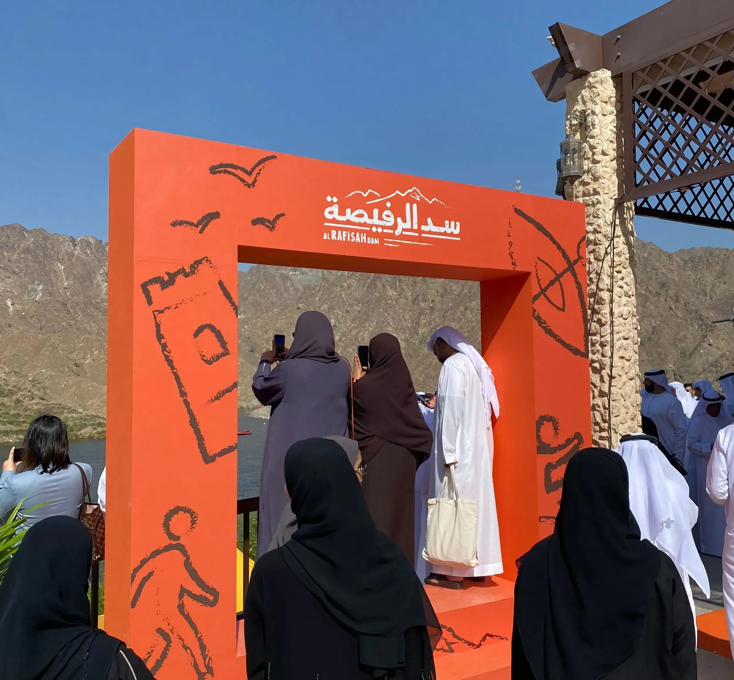 Visitors at the Al Rafisah Dam brand launch event, interacting with a large, orange photo frame featuring the destination's logo and branding elements. This image captures the successful brand activation by Skyne.