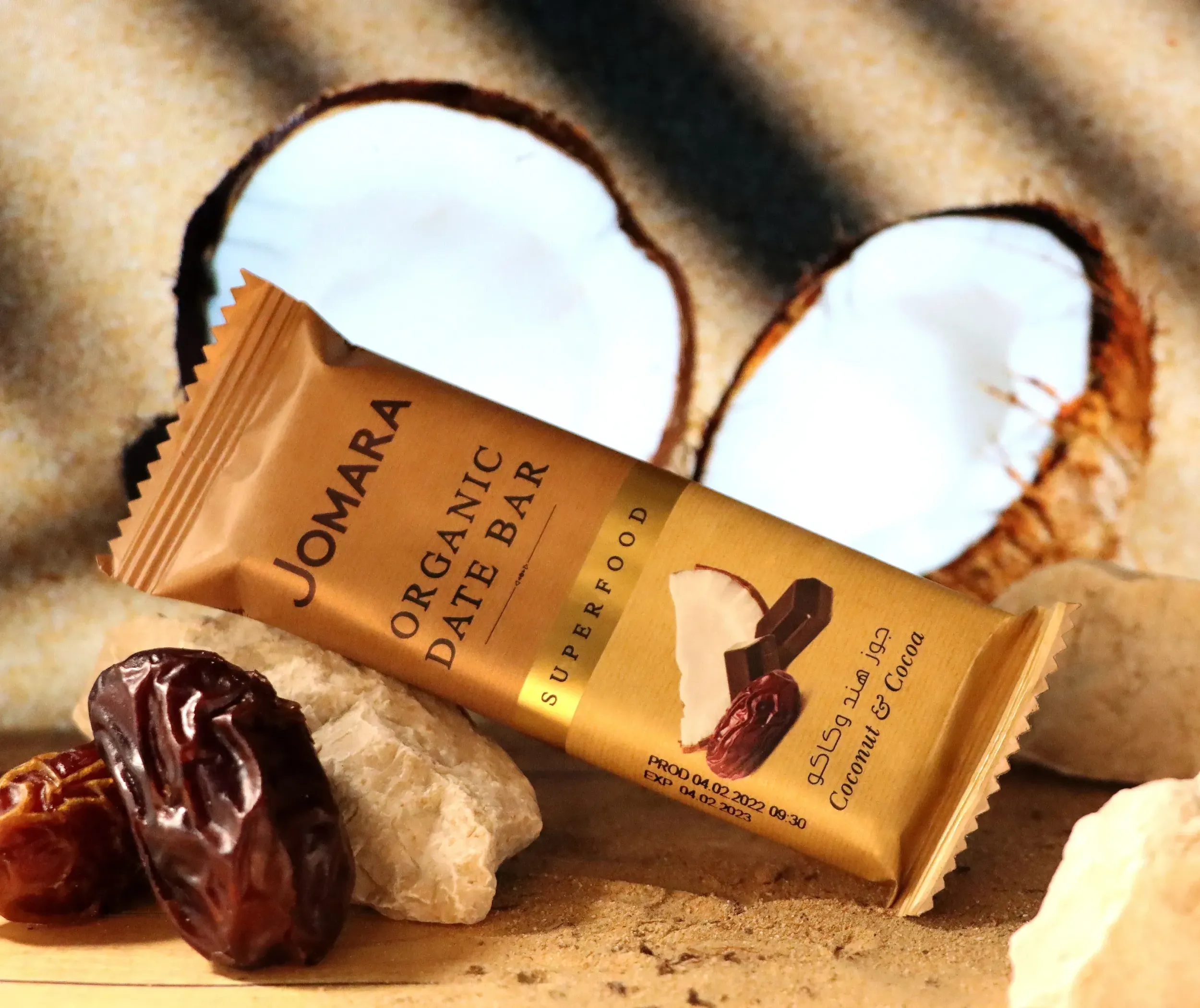 Jomara organic date bar with dates and coconut on desert sand background