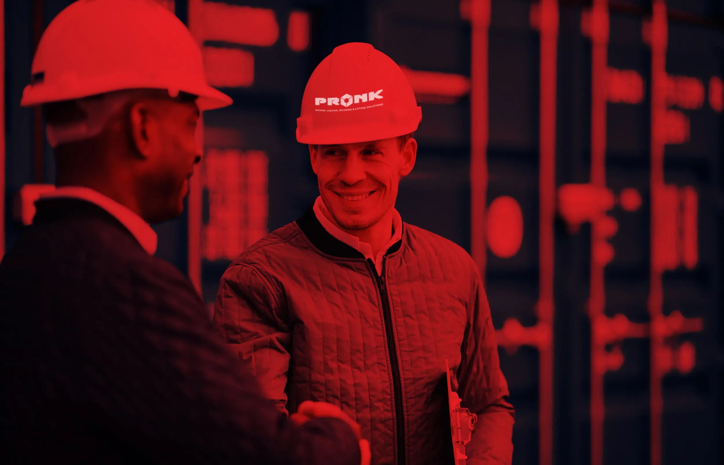 Two men in hard hats, one with a Pronk branded hard hat, shaking hands in a red-tinted industrial setting. Skyne emphasizes strong partnerships in its branding strategies for businesses in Dubai, Riyadh, and Jeddah.