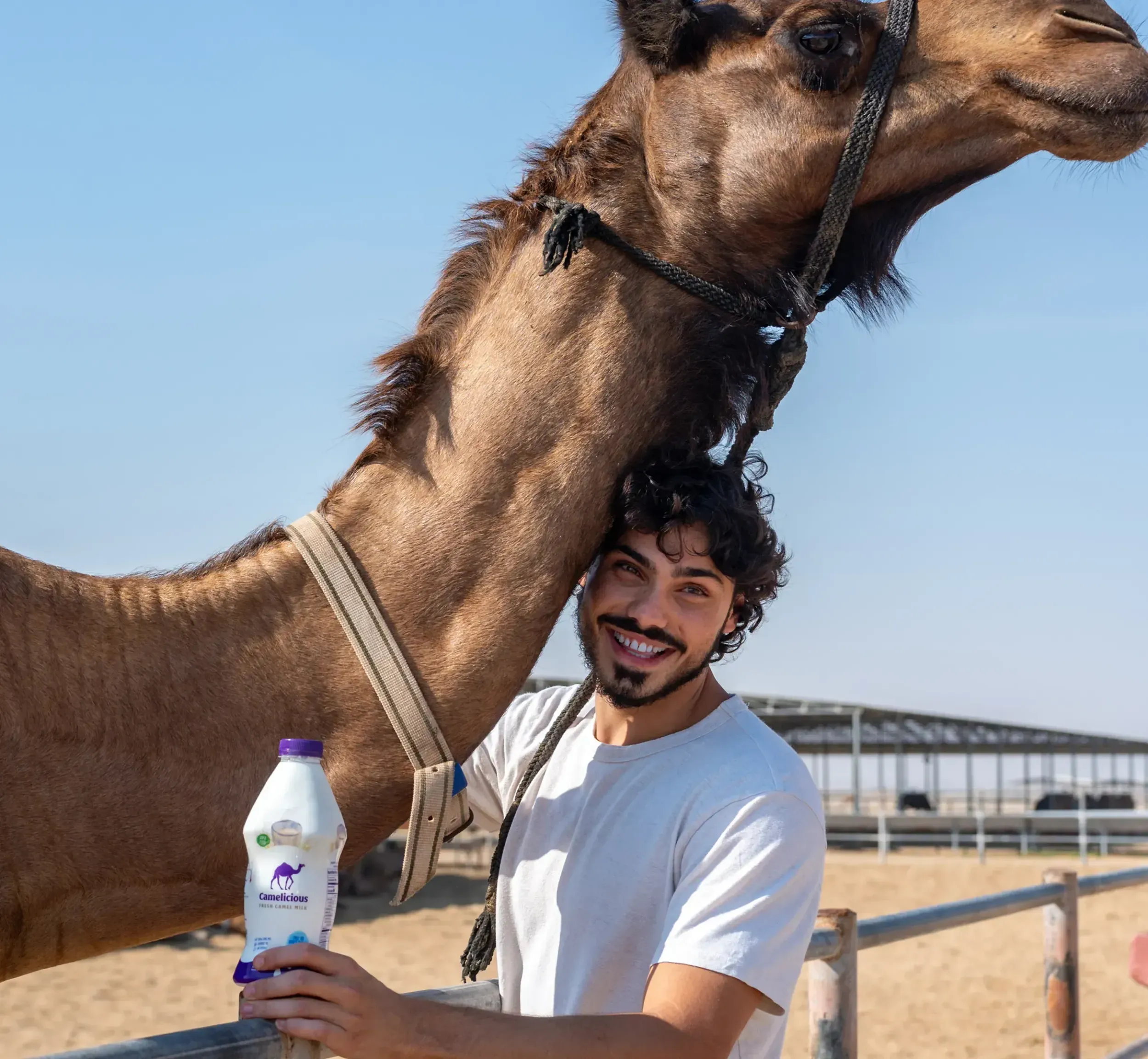 A man smiling with a camel and holding a Camelicious milk bottle, showcasing the authentic connection to the product's origin and Skyne's ability to create compelling branding narratives for food and beverage.