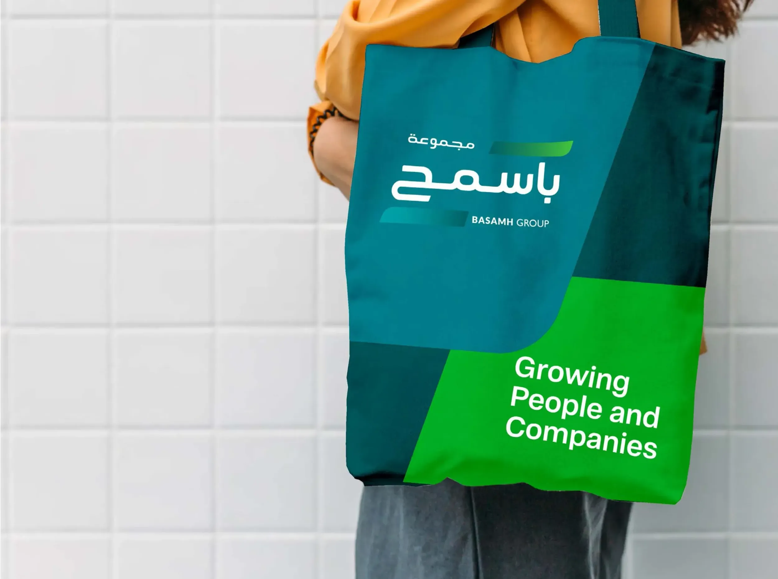 A person holding a Basamh Group branded tote bag with the slogan "Growing People and Companies." Skyne, a branding agency, designed promotional materials that reflect the company's values.
