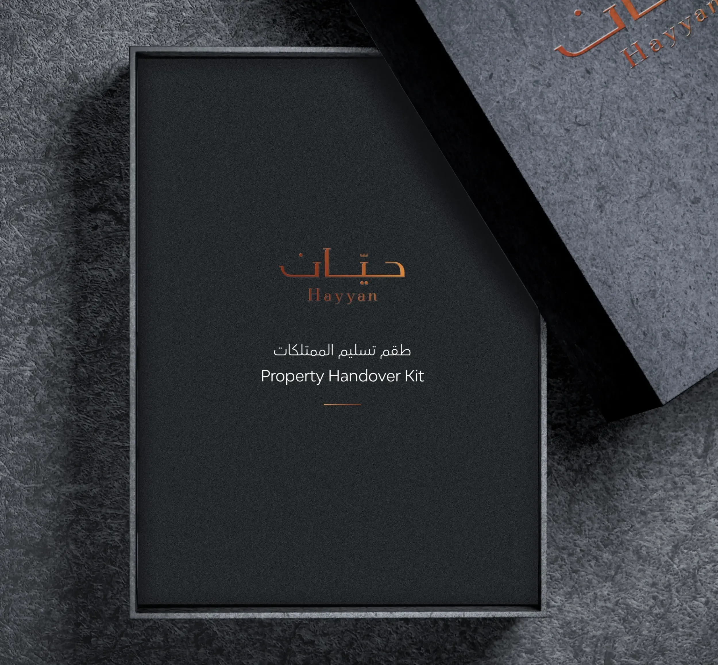 Elegant black Hayyan Property Handover Kit box with bilingual text and copper-foil logo on textured surface.
