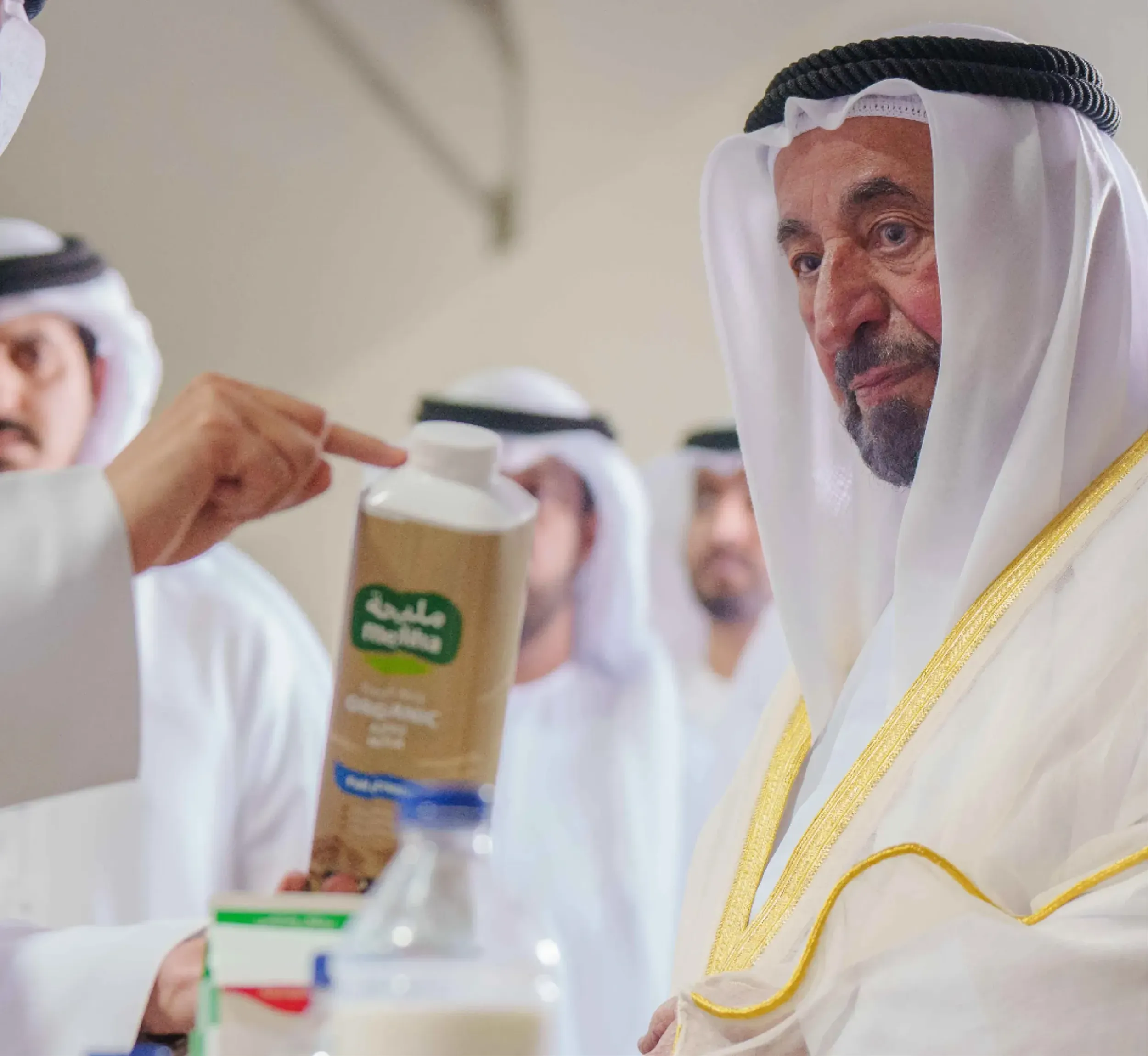 A man in traditional Middle Eastern attire listens to another person holding a carton of milk