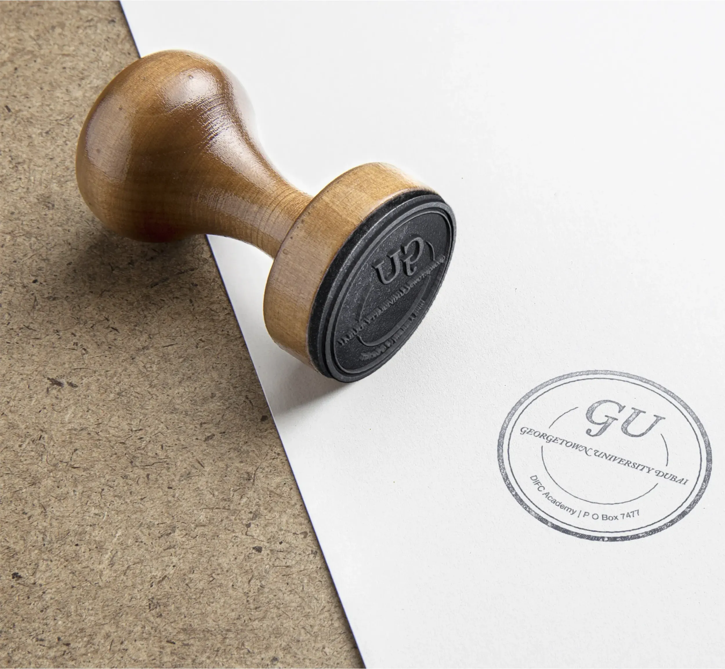 Wooden handle rubber stamp with Georgetown University Dubai circular logo imprint on paper. Skyne ensures meticulous attention to detail in brand identity and official documentation for educational institutions in Dubai, Riyadh, and Jeddah.